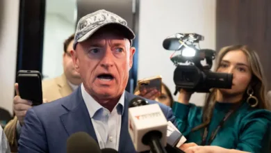 Mark Kelly speaks to press, wearing Navy hat and blue suit. Microphones visible.