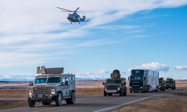 Military convoy with armored vehicles and helicopter on road.