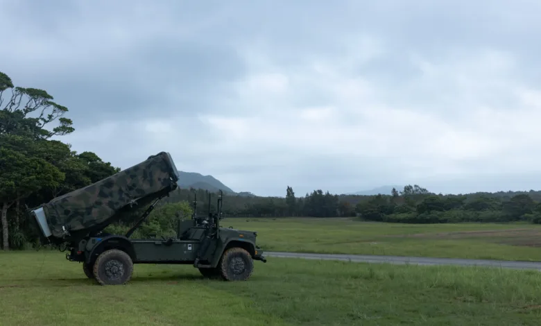 Military missile launcher on vehicle in field against cloudy sky.