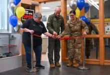 Ribbon cutting ceremony with three people and balloons at an opening.