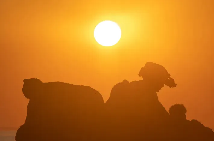 Silhouette of people on rocks against a bright orange sunset.