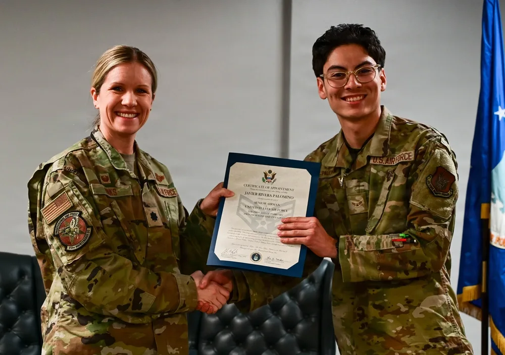 Air Force officer shaking hands, presenting certificate to Airman Palomino.