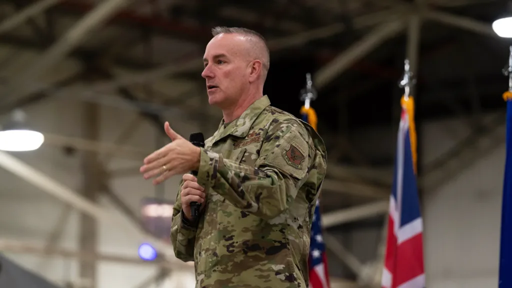 Air Force officer speaks at event, gesturing with hand and holding a microphone.