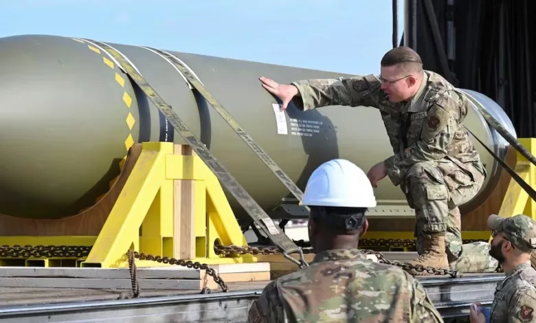 Airmen inspecting a large bomb secured on a trailer with yellow supports.