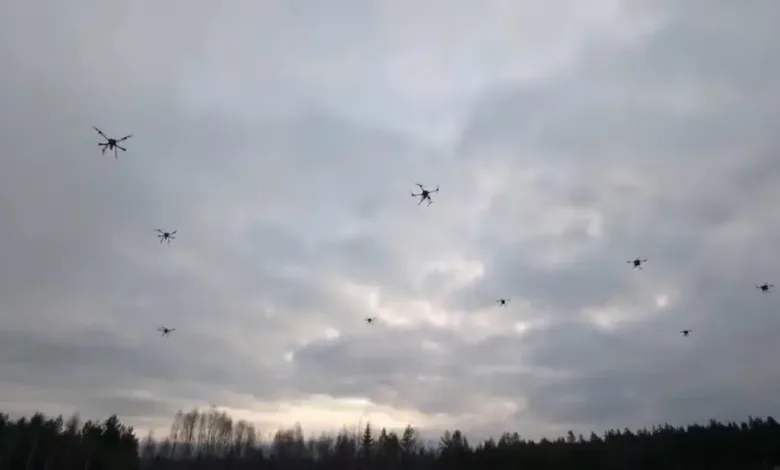 Swarm of drones flying in cloudy sky over forest.