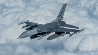 F-16 Fighting Falcon fighter jet flying through clouds, SP tail code, armed with missiles.