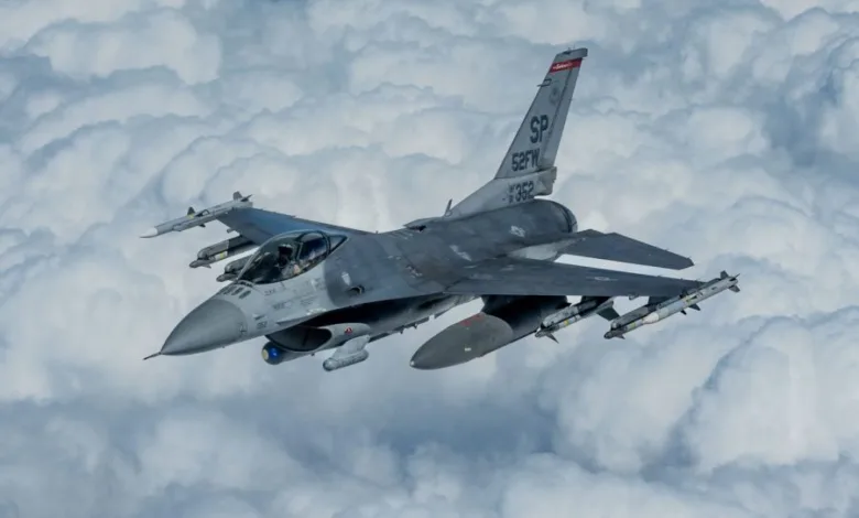 F-16 Fighting Falcon fighter jet flying through clouds, SP tail code, armed with missiles.