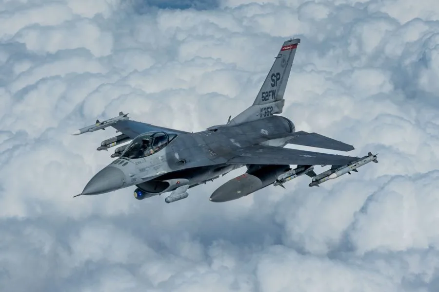 F-16 Fighting Falcon fighter jet flying through clouds, SP tail code, armed with missiles.
