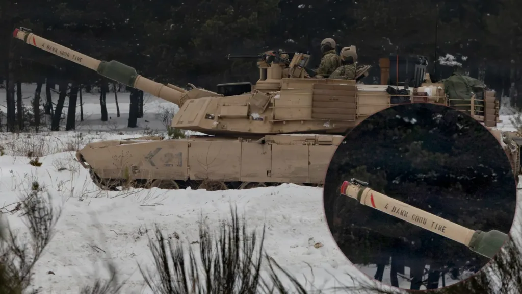 M1 Abrams tank in snow with "A Dark Good Time" written on the barrel. Soldiers visible in turret.