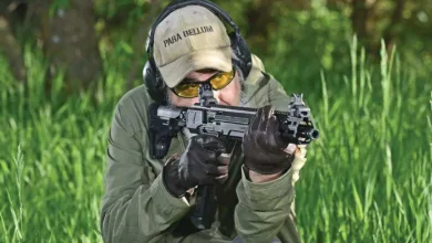 Man firing compact submachine gun with "Para Bellum" hat and ear protection.