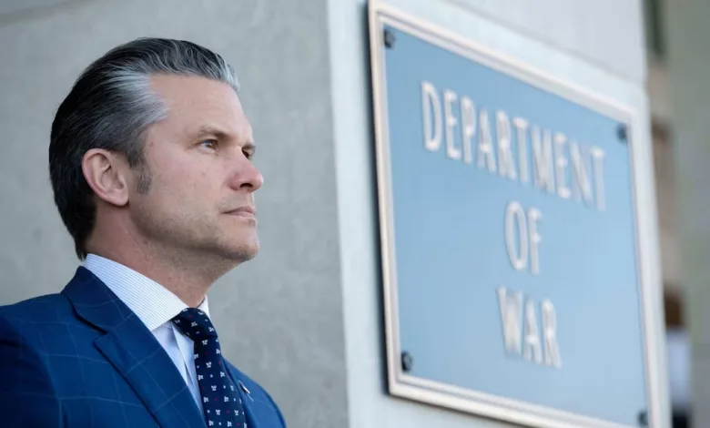 Man in suit by Department of War sign. Gray hair, serious expression.