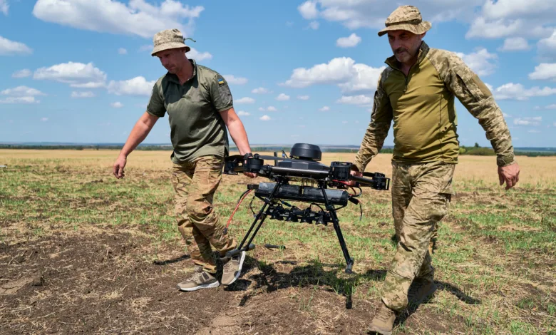 Two men carry a large drone across a field on a sunny day.