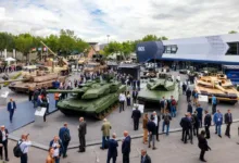 Military tanks on display at defense industry trade show with crowds of people.