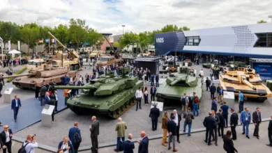 Military tanks on display at defense industry trade show with crowds of people.