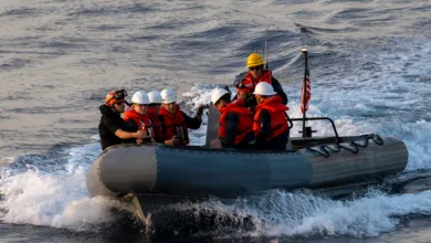 Navy personnel in rigid-hulled inflatable boat on water, wearing life vests and helmets.