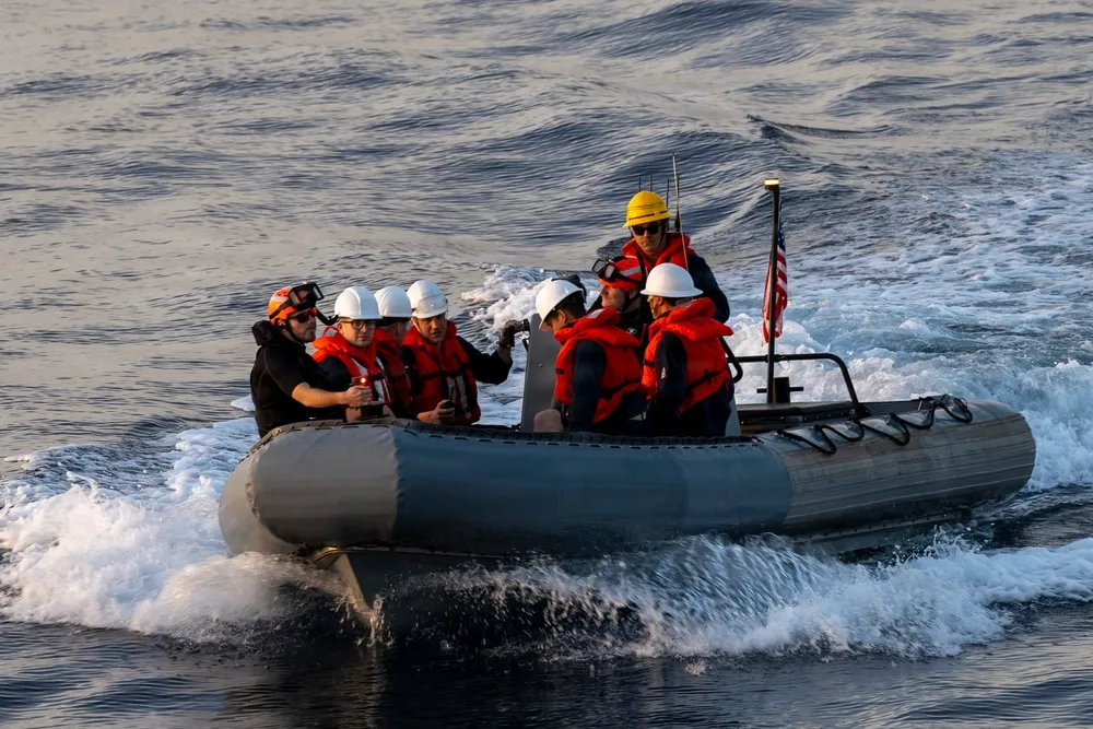 Navy personnel in rigid-hulled inflatable boat on water, wearing life vests and helmets.
