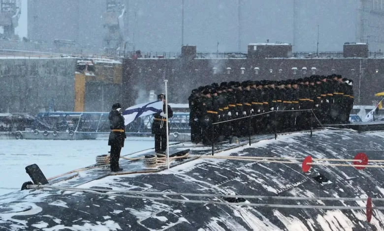 Russian Navy sailors on a submarine during a flag raising ceremony in snowy conditions.