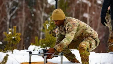 Soldier prepares drone for flight in snowy field, wearing military camouflage.