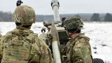Soldiers load artillery shell into howitzer in snowy field exercise.