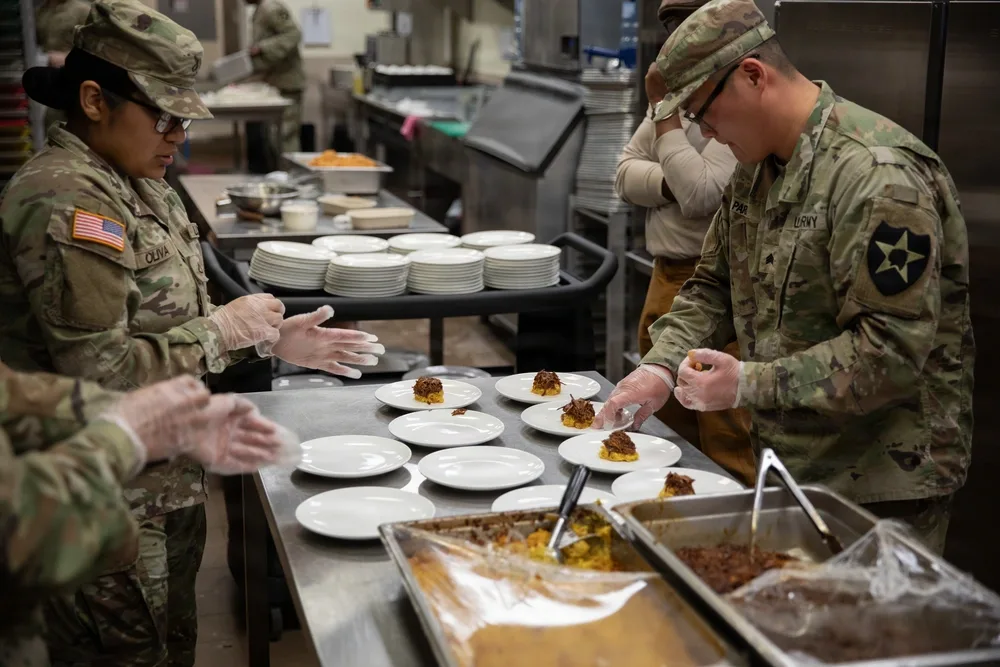 Soldiers preparing food in a military kitchen, serving plates.