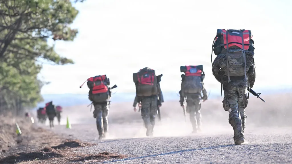 Soldiers rucking with heavy packs on dusty trail. Military training exercise.