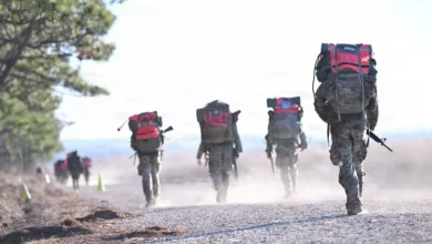 Soldiers rucking with heavy packs on dusty trail. Military training exercise.