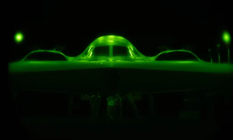 Green night vision image of a stealth bomber aircraft on a runway with ground crew.