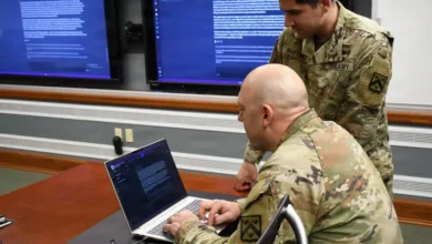 Two U.S. Army soldiers reviewing documents on laptop in a conference room.