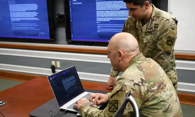 Two U.S. Army soldiers reviewing documents on laptop in a conference room.