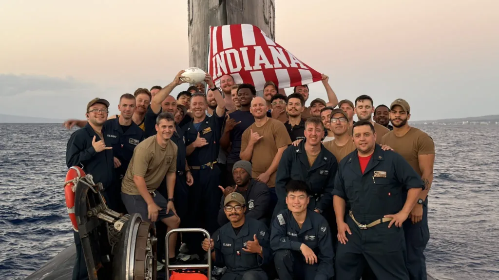 US Navy sailors on submarine with "Indiana" flag, smiling at the camera.