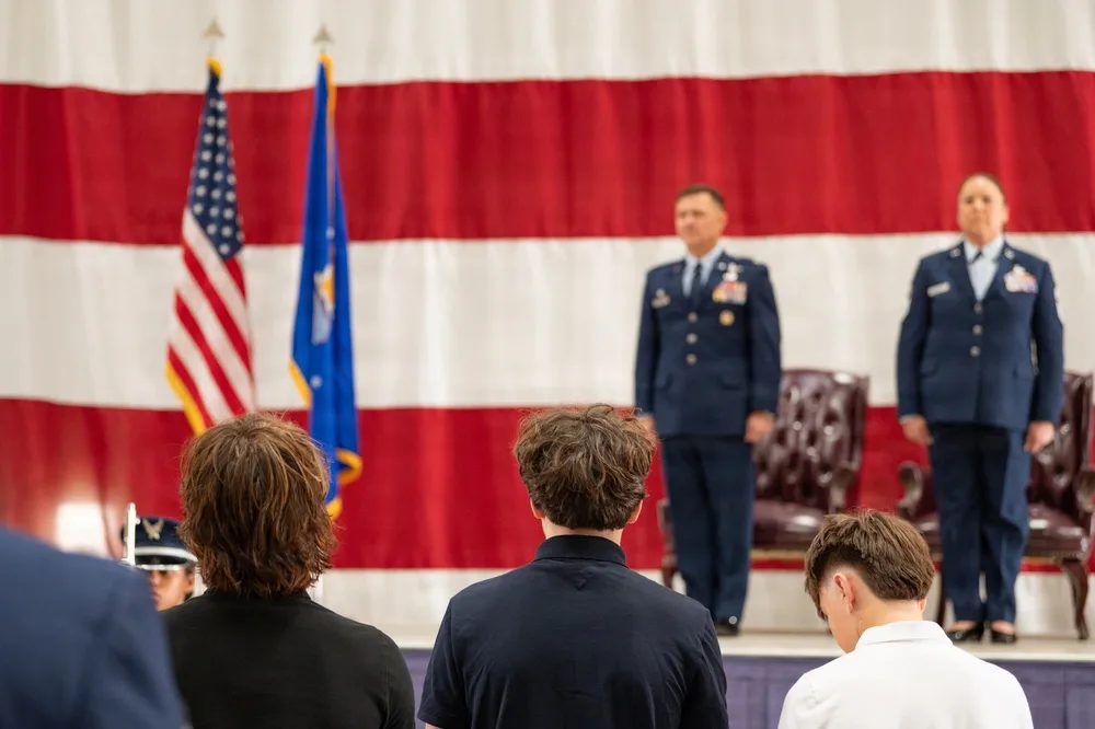 Air Force officers on stage during a ceremony with US flag backdrop.