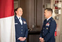 Two Air Force officers in uniform, smiling and facing each other indoors.