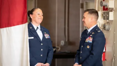 Two Air Force officers in uniform, smiling and facing each other indoors.