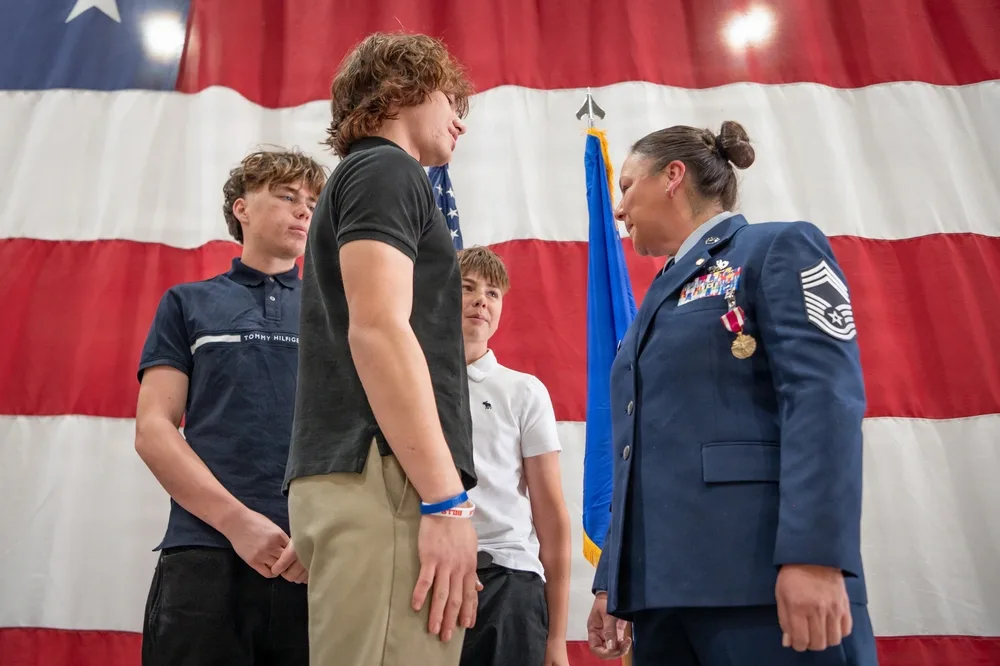Air Force officer speaks to young men at retirement ceremony with US flag backdrop.
