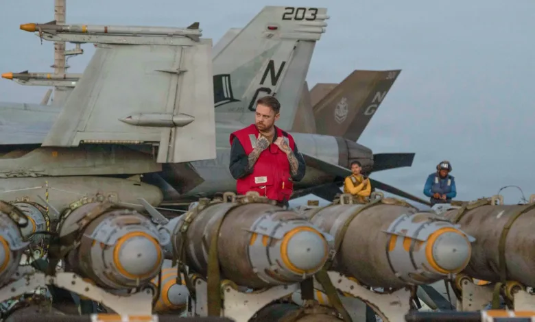 Aircraft carrier deck crew with bombs and fighter jets, possibly related to Iran strikes.