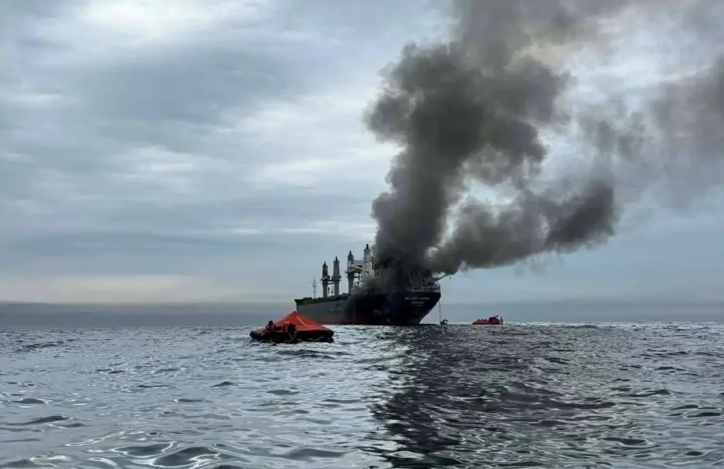 Burning cargo ship with lifeboats in the ocean, dark smoke plume visible.