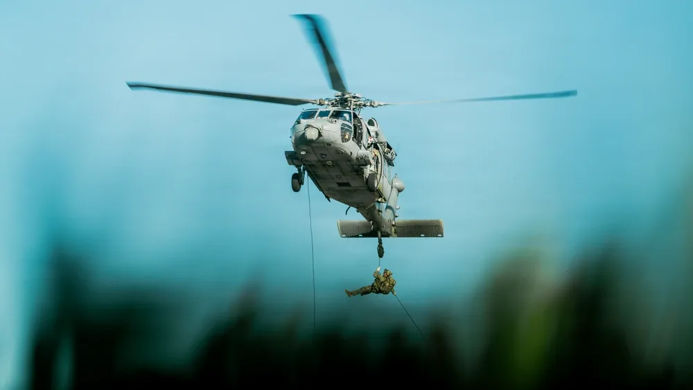 EOD technician rappelling from a helicopter during daytime training exercise.