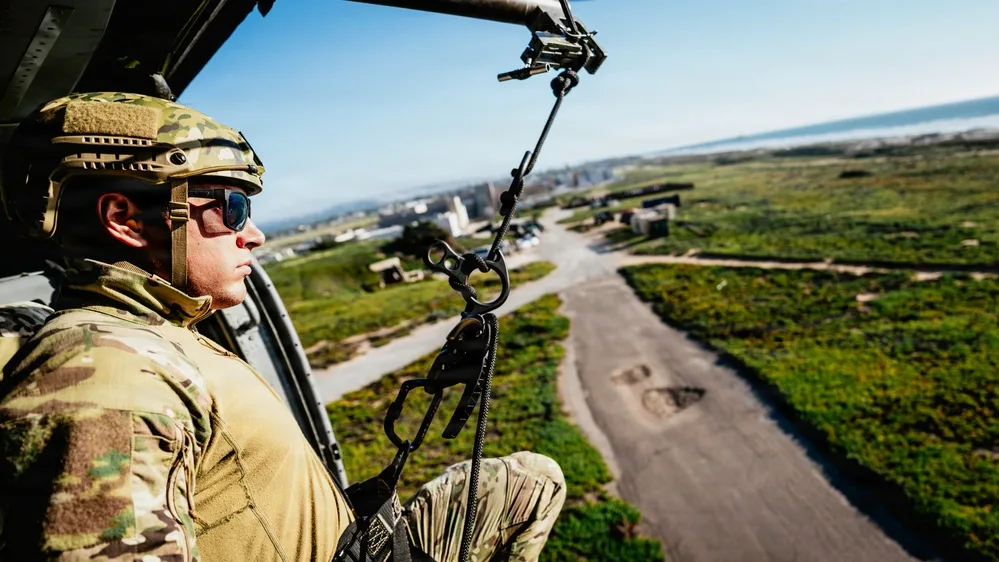 EOD technician rappelling from helicopter during daytime training exercise.