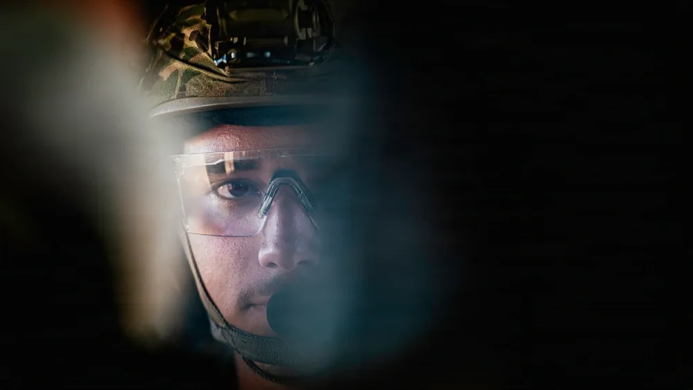 EOD technician in helmet and safety glasses with rappelling gear. Focus on face.