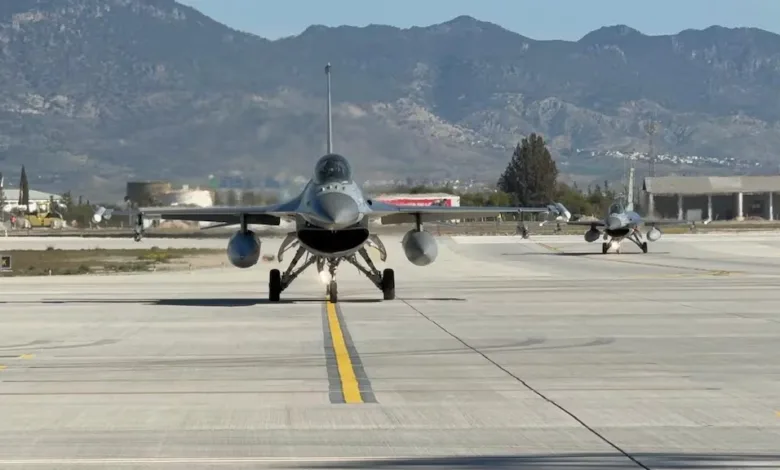 Two F-16 fighter jets taxiing on runway with mountains in background.