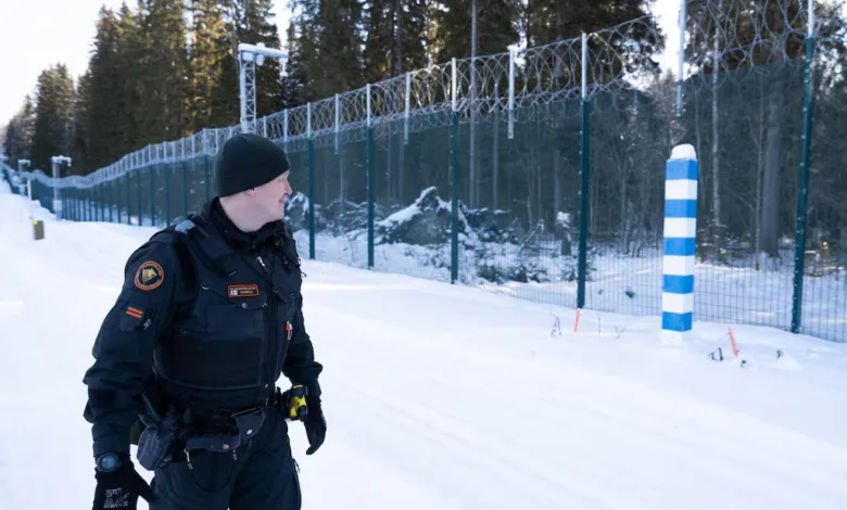 Border guard patrolling snowy Finnish-Russian border with security fence.