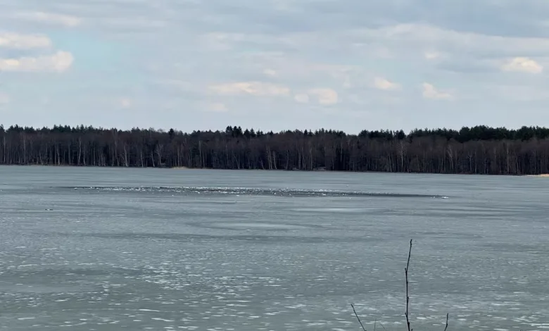 Frozen lake with thin ice and distant trees under a cloudy sky.