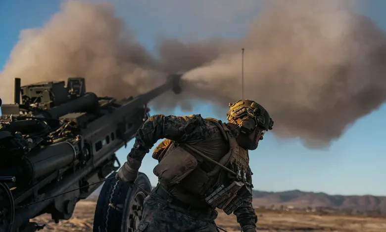 Marine firing M777 howitzer with smoke and desert backdrop.