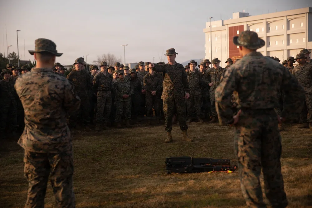 Marines in camouflage gather outdoors for briefing at MCAS Iwakuni HHS supply hike.