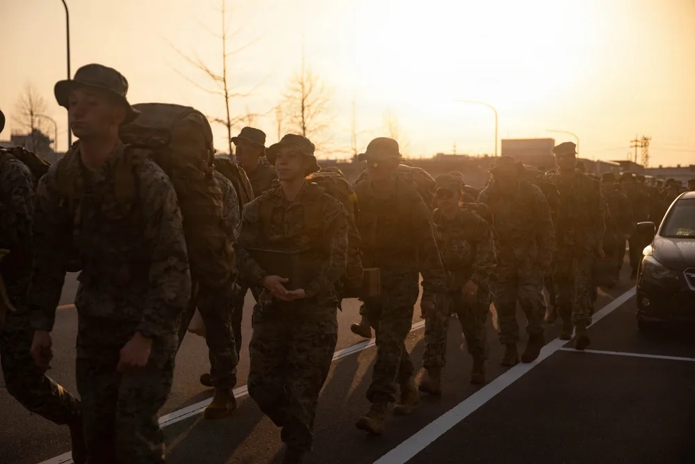 US Marines hike at MCAS Iwakuni wearing camouflage and carrying rucksacks.