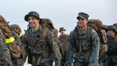 Marines hike with packs at MCAS Iwakuni, wearing camouflage uniforms and hats.