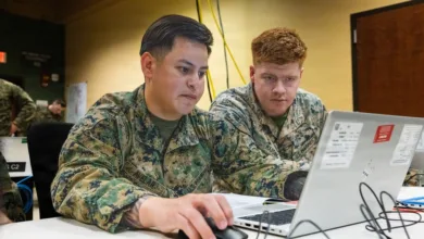 Two Marines working on a laptop, reviewing data at a table.