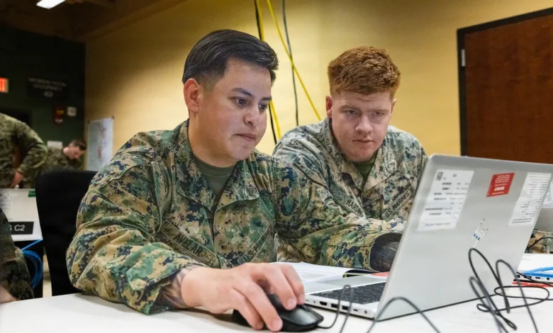 Two Marines working on a laptop, reviewing data at a table.