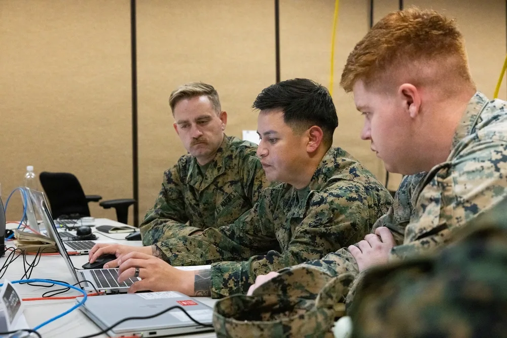 Three Marines working at laptops in a training exercise.