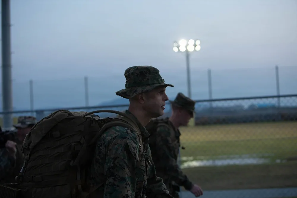 Marines hike with heavy packs at MCAS Iwakuni, wearing camouflage and boonie hats.